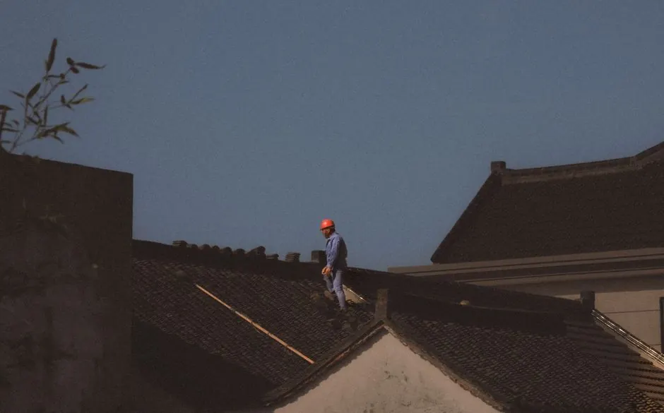 A construction worker with a red helmet standing on a roof on a clear day.